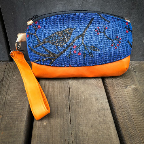 Une petite pochette zippée cousue en cuir orange et une écharpe de portage bleu électrique, noir et rouge avec un motif d'oiseaux dans des branches'.