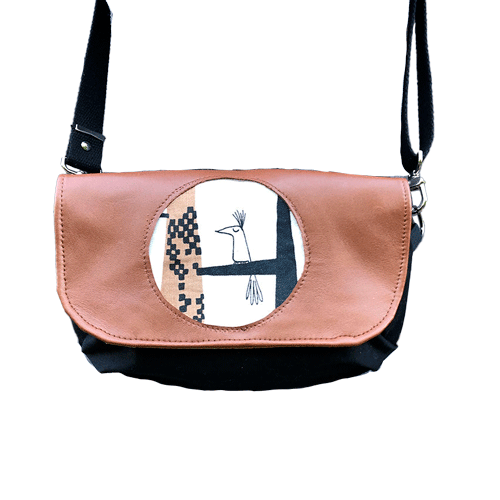 Une pochette à rabat cousue en cuir caramel, satin noir et tissu à motifs design suédois, doublée de popeline jaune.