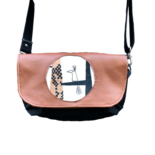 Une pochette à rabat cousue en cuir caramel, satin noir et tissu à motifs design suédois, doublée de popeline jaune.