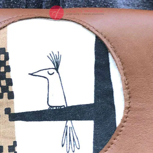 Une pochette à rabat cousue en cuir caramel, satin noir et tissu à motifs design suédois, doublée de popeline jaune.