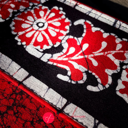 A flat handbag with a flap made of black, white, and red batik cotton fabric.