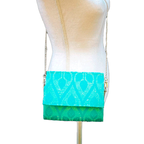 Un sac à main plat avec un rabat en écharpe de portage crème et turquoise avec motif de feuilles stylisées.
