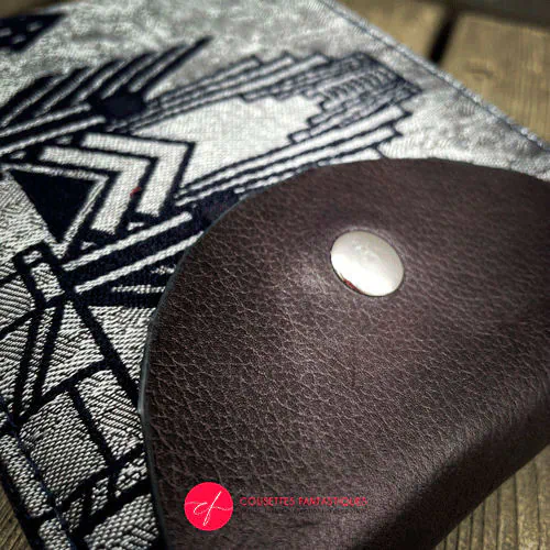Un portefeuille fabriqué à partir d'une écharpe de portage pour bébé à motifs géométriques Art Déco bleu nuit et argent, en cuir bleu nuit, gabardine bleu nuit, et popeline gris souris.