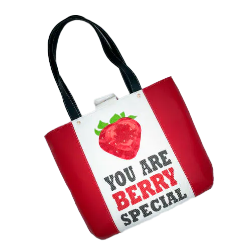 Un grand sac fait à l'extérieur de simili rouge et d'une toile imprimée d'un dessin de fruit avec un jeu de mots en anglais dessous, et à l'intérieur d'une popeline rouge vif.