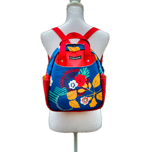 Un sac à dos fait en toile bleue roi à motifs floraux jaunes, blancs et rouges et toile rouge gaufrée à l'extérieur, popelines unies rouges et jaunes à l'intérieur.