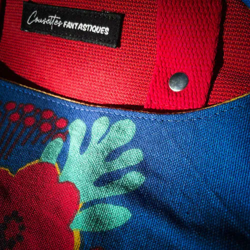 Un sac à dos fait en toile bleue roi à motifs floraux jaunes, blancs et rouges et toile rouge gaufrée à l'extérieur, popelines unies rouges et jaunes à l'intérieur.