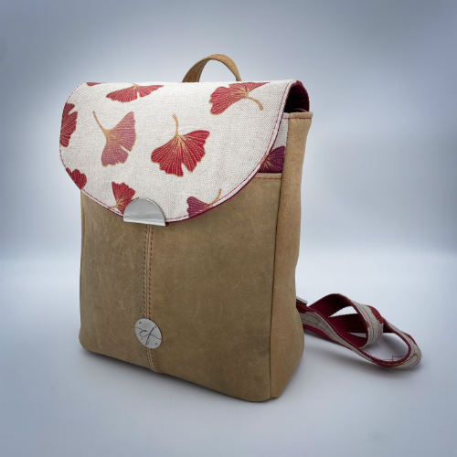 Un sac à dos fait d'un cuir de couleur camel et d'une toile en polycoton avec un motif de feuilles de Ginkgo Biloba rouges.