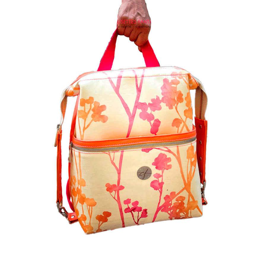 Un sac à dos confectionné en simili orange vif et en tissu d'ameublement crème au motif végétal dégradé de rose à orange.