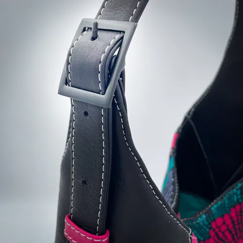 Un sac d'épaule fabriqué à partir d'un coupon de tissu façon wax et de chutes de cuir noir et rose, et doublé d'une doublure turquoise.