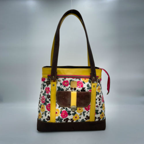 Un sac d'épaule fabriqué à partir de cuirs chocolat et jaune mariés à une toile fleurie avec des fleurs roses et jaunes.
