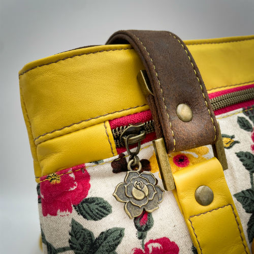 Un sac d'épaule fabriqué à partir de cuirs chocolat et jaune mariés à une toile fleurie avec des fleurs roses et jaunes.
