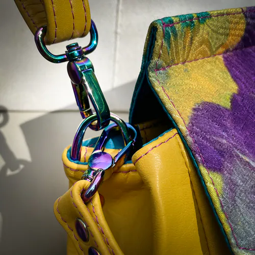 Un sac anguleux confectionné avec un cuir jaune et un tissu damassé peint, avec une doublure en satins turquoise et violet.