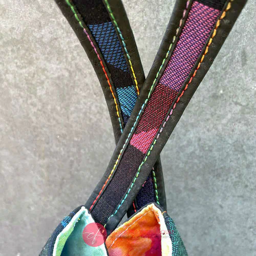 Un sac d'épaule fabriqué avec une écharpe de portage noire à motif géométrique arc-en-ciel et du liège noir, avec un intérieur en tourbillon arc-en-ciel lumineux.