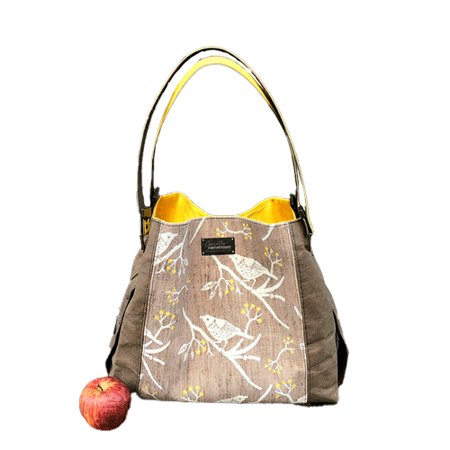 Un sac d'épaule fait à partir de papier lavable couleur chocolat, écharpe de portage beige rosé chiné, au motif d'oiseaux blancs dans des branchages blancs et jaune, avec une doublure jaune vif.