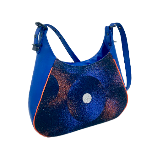 Un sac d'épaule zippé, fabriqué à partir de chutes d'une écharpe de portage noir, bleu, rose et orange et de simili bleu royal, et doublé d'une doublure orange vif lumineuse.