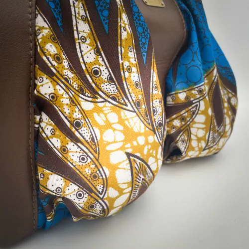 Un sac d'épaule composé de cuir de chèvre marron, de wax bleu et moutarde et d'une doublure jaune moutarde.