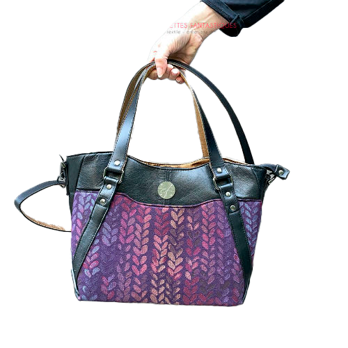 Un sac d'épaule fait en tissu dans les tons violets, pourpres, roses... au motif de goutelettes, et de cuir d'agneau noir upcyclé.