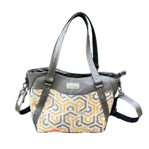 Un sac d'épaule fait en écharpe de portage gris, moutarde et écru avec motifs géométriques, et cuir d'agneau gris.