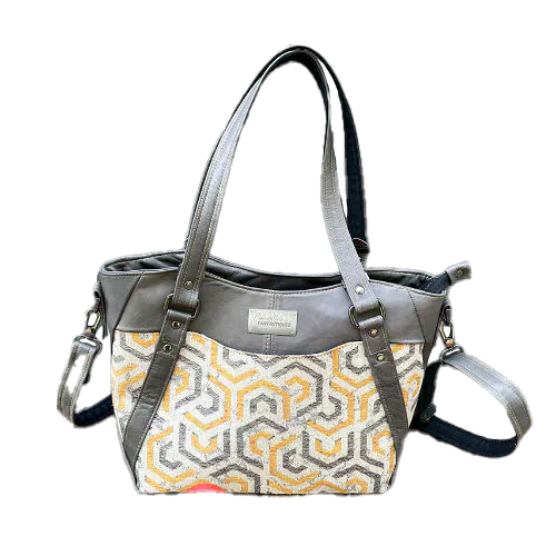 Un sac d'épaule fait en écharpe de portage gris, moutarde et écru avec motifs géométriques, et cuir d'agneau gris.