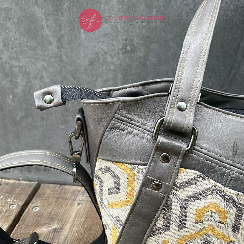 A shoulder bag made from gray, mustard, and ecru babywearing wrap with geometric patterns, and gray lamb leather.