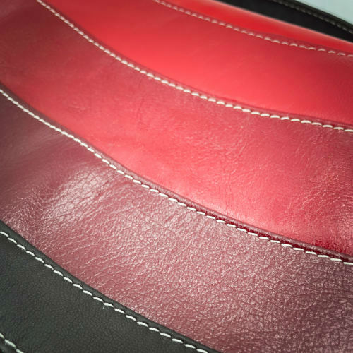 Un sac d'épaule composé de cuirs de différentes teintes de rouge, un marron et une doublure rouge.