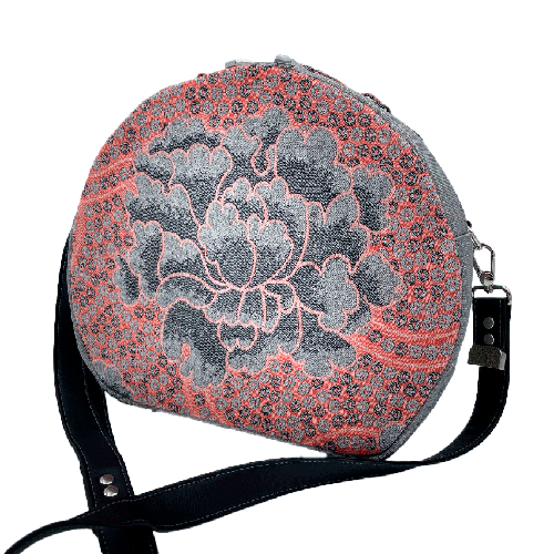 Un sac d'épaule rond composé de toile vinyl grise à paillettes, d'un coupon d'écharpe de portage rose et gris au motif floral vintage et une doublure satinée grise.