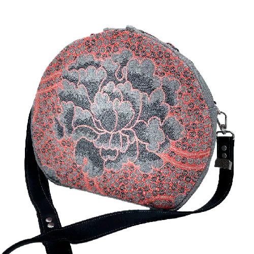 Un sac d'épaule rond composé de toile vinyl grise à paillettes, d'un coupon d'écharpe de portage rose et gris au motif floral vintage et une doublure satinée grise.