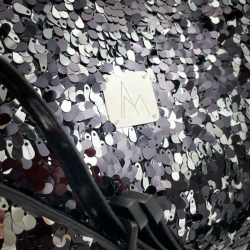 Un grand sac d'épaule fabriqué à partir d'un tissu à sequins noirs et argents, un denim couture gris et un simili fin noir.