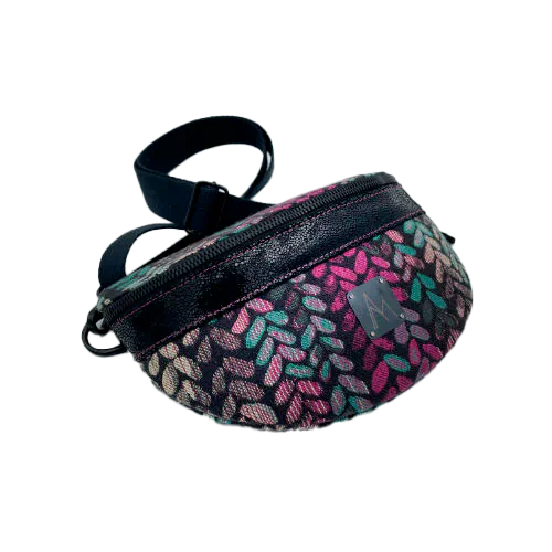 Une banane cousue dans un cuir vernis noir et une chute d'écharpe de portage au motif de mailles vertes, beiges et roses sur fond noir, couplés à une popeline rose vif à l'intérieur.