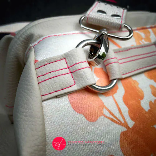 Un petit sac à main constitué de simili crème et tissu d'ameublement crème, au motif végétal dégradé de rose à orange.