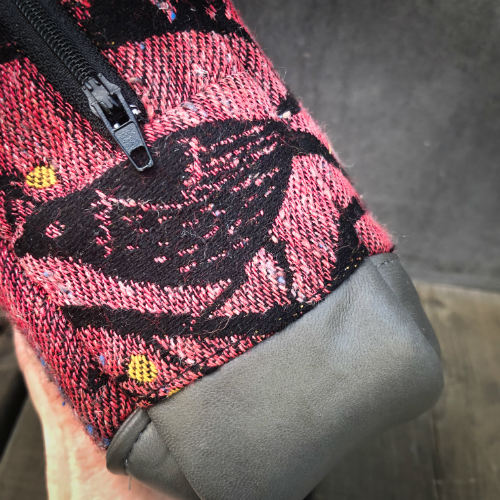 Un mini sac à main fabriqué à partir de chutes d'écharpe de portage montrant des oiseaux dans un arbre dans des tons roses et noirs, et du cuir d'agneau gris.