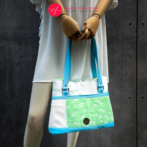 A handbag made of light blue leather and white, light blue, and apple green fabric with a bird motif.