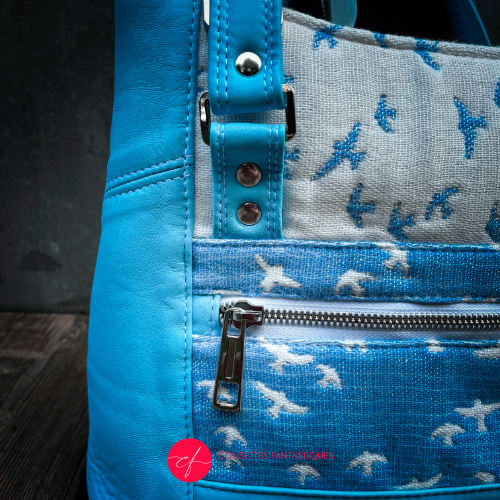 A handbag made of light blue leather and white, light blue, and apple green fabric with a bird motif.