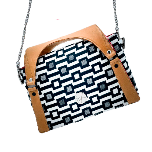 Un sac à main fait en écharpe de portage noir et blanc motif géométrique, cuir caramel et popeline rouge.