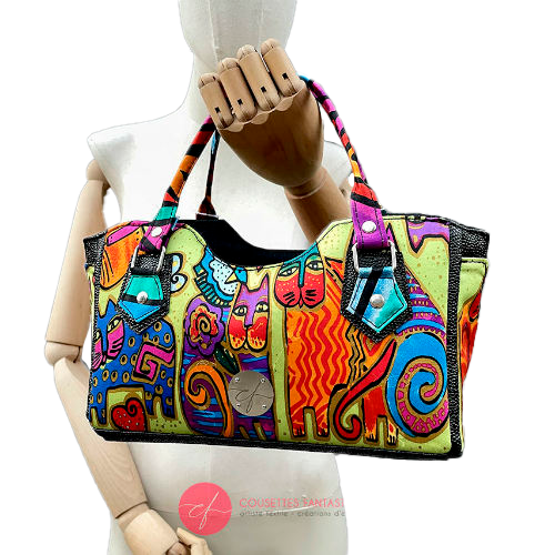 Un petit sac à main constitué d'un simili noir brillant texture galuchat et d'un foulard de soie au motif de chats très colorés.