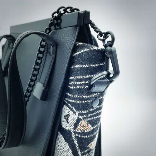 Un petit sac à main confectionné à partir d'écharpe de portage au motif de macareux dans des vagues stylisées dans des tons noirs, blancs et orange, et du simili noir.