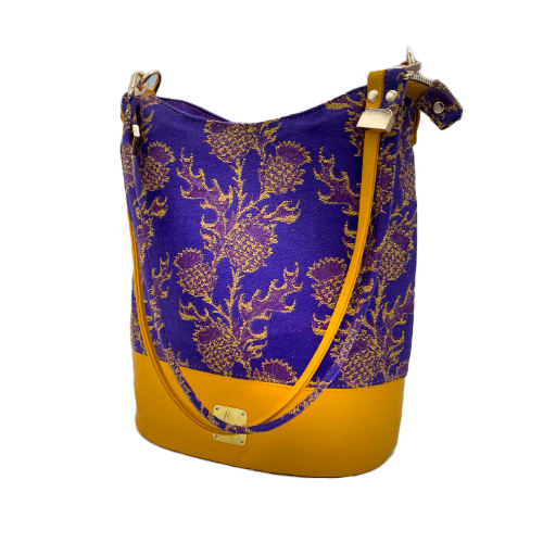 Un sac seau fabriqué avec de l'écharpe de portage au motif de chardons jaunes sur fond violet et du cuir d'agneau jaune.