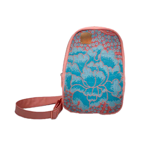 Un sac à dos fait de simili coloris pêche et d'une écharpe de portage dans les tons rose et turquoise avec un motif floral vintage.