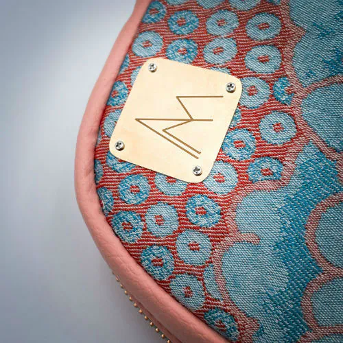 Un sac à dos fait de simili coloris pêche et d'une écharpe de portage dans les tons rose et turquoise avec un motif floral vintage.