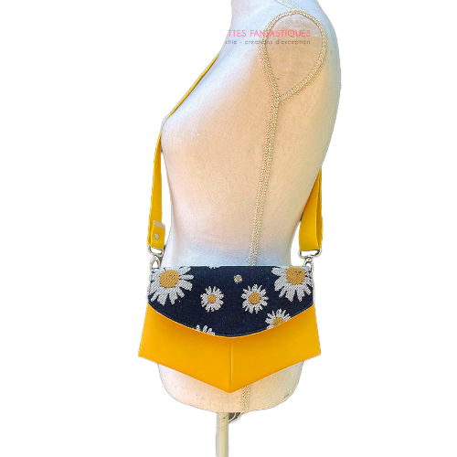 Un petit sac en simili jaune et un coupon de tissu d'écharpe avec des marguerites blanches et jaunes sur un fond bleu marine.
