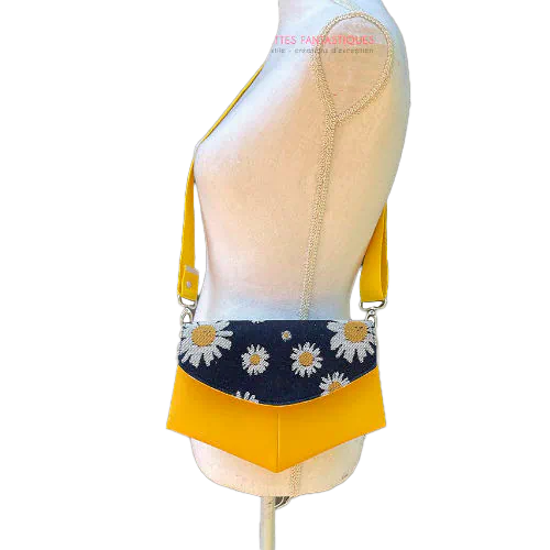 Un petit sac en simili jaune et un coupon de tissu d'écharpe avec des marguerites blanches et jaunes sur un fond bleu marine.