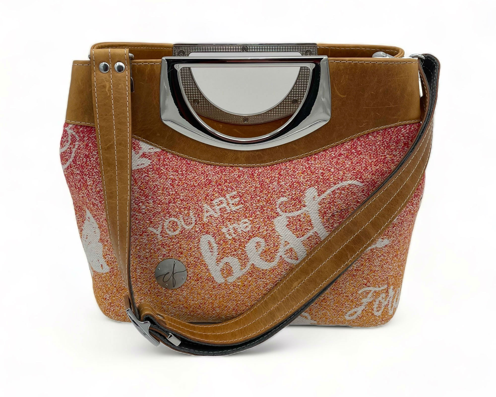 'Empuissancement', an ultra-luxury shoulder bag with its high-quality materials and meticulous finishes. A masterpiece about women, reflecting both their strength and delicacy, sophistication, and simplicity. Made of organic-certified caramel-colored cowhide and a babywearing wrap with inspiring white text on a gradient background of summer colors.