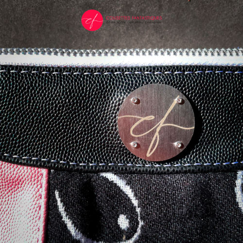 A messenger bag made from a black and white babywearing wrap with stylized breast drawings, black stingray leather, and pink stingray leather.