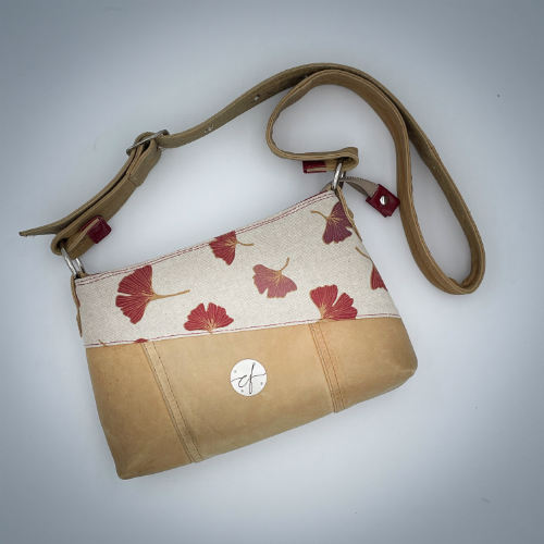 A rectangular crossbody bag made from camel colored leather and a red Ginkgo Biloba leaves patterned polycotton canvas.