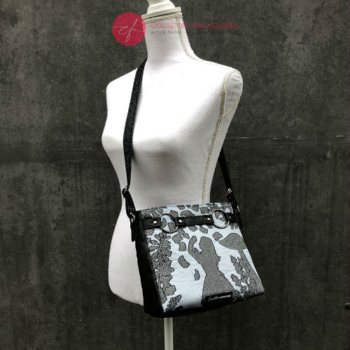 A trapezoid crossbody bag made from a black, gray-blue, and silver “Alice in Wonderland” babywearing scarf, paired with hand-quilted black faux leather.