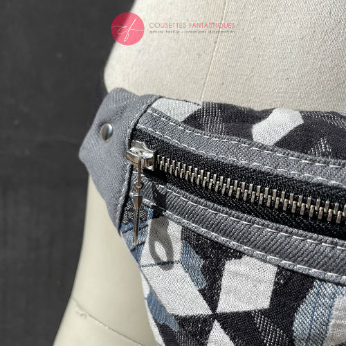 A fanny pack made from babywearing fabric in gray, white, and blue tones with a floral and geometric pattern and gray denim.
