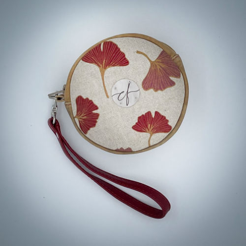 A round pouch made of camel colored leather and a red Ginkgo Biloba leaves patterned polycotton canvas.
