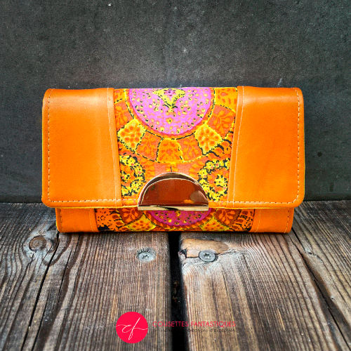 A wallet made of orange lambskin leather and vintage multicolored rayon, in shades of orange, yellow, and pink.