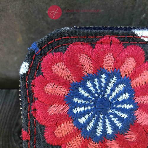 A small zippered card and coin holder made of gray fabric embroidered with blue, red, and white Scandinavian floral patterns.