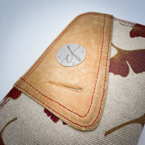 A zippered card and coin holder made with camel colored goat leather and a red Ginkgo Biloba leaves patterned polycotton canvas.